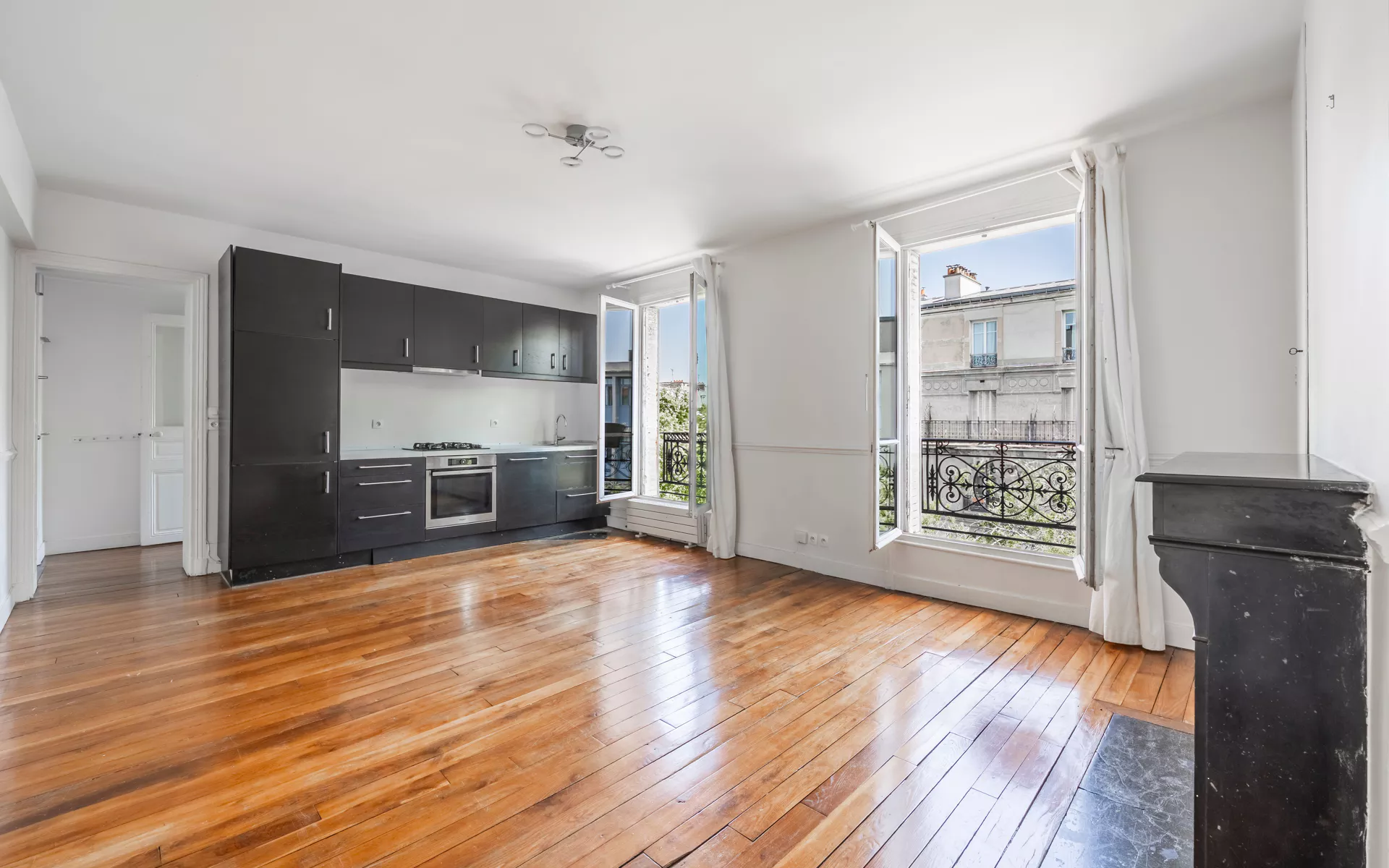 Séjour lumineux d'un appartement ancien parisien - parquet, cheminée en marbre et vue sur les façades haussmanniennes